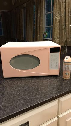 a pink microwave oven sitting on top of a kitchen counter next to a bottle of deodorant