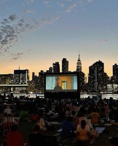 people are sitting on the grass watching a movie in front of a cityscape