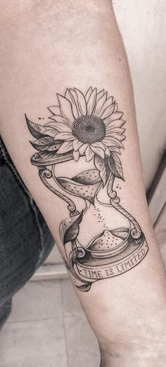 a woman's leg with a sunflower and an hourglass tattoo on it