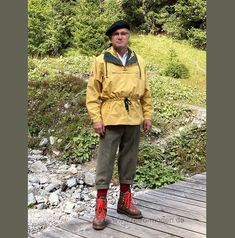 a man standing on a wooden bridge wearing raincoats and red boots with trees in the background