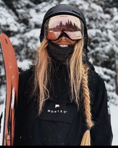 a man with long blonde hair wearing skis and a black hoodie holding his snowboard