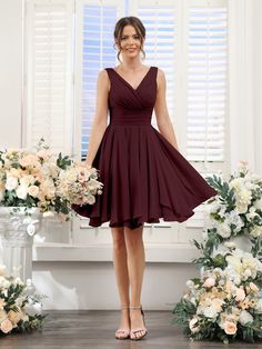 a woman standing in front of flowers wearing a maroon bridesmaid dress and heels