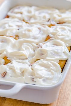 a casserole dish with white icing and cinnamon rolls in it on a wooden table