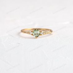 a gold ring with an oval cut green stone and diamonds on the side, sitting on a white surface