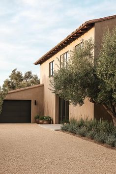 a large house with an olive tree in the front yard and two garages on each side