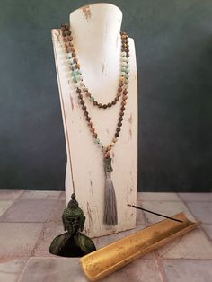 This beautiful Mala Necklace is made with 108 beads of Amazonite, Tiger's Eye, and Picture Jasper, each with its own unique healing properties. The Accent Dzi beads are believed to have protective and healing properties. This Mala necklace is not only a stunning accessory but also a tool for meditation and mindfulness. The necklace is hand-knotted between each bead and finished with a tassel under the Dzi beads.Materials & style:- 108 beads for traditional Mala use- Dzi beads for spiritual signi Spiritual Round Beads Crystal Necklaces For Layering, Spiritual Crystal Necklaces With Round Beads For Layering, Spiritual Gemstone Beads Necklace For Layering, Spiritual Round Beads Necklaces For Layering, Handmade Spiritual Necklace For Layering, Earthy Crystal Necklaces With Natural Stones For Healing, Earthy Crystal Necklaces For Healing With Natural Stones, Spiritual Beaded Necklaces For Layering, Spiritual 108 Beads Necklace For Meditation