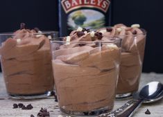 three glasses filled with chocolate desserts on top of a wooden table next to a bottle of bailey's