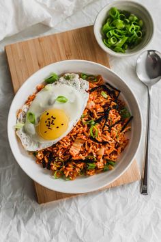 an egg is sitting on top of rice in a white bowl next to a spoon