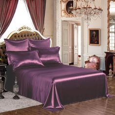 a bed with purple sheets and pillows in a room next to a chandelier