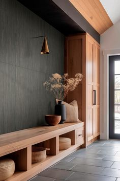 a wooden shelf with vases and plants on it in front of a black wall