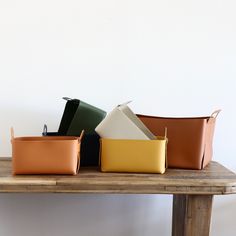 four different colored leather baskets sitting on top of a wooden table next to a white wall