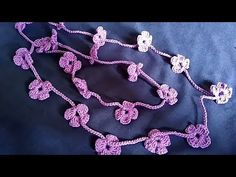 a crocheted necklace with flowers is laying on a blue cloth and it looks like something out of space