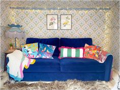 a blue couch with many pillows on it in front of a wallpapered room