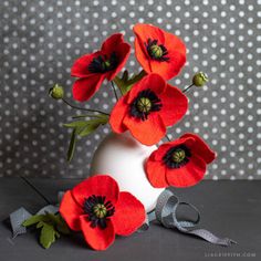 three red flowers in a white vase on a gray table with polka dot wallpaper