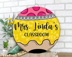 a sign that says mrs linda's classroom on the side of a table next to a potted plant