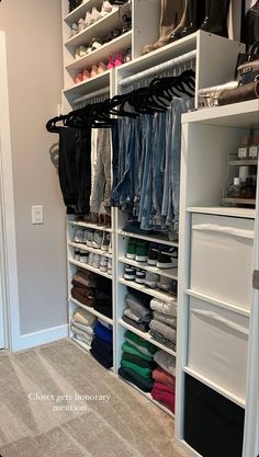 an organized closet with white shelving and lots of clothes hanging on the shelves in front of it