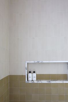 two bottles are sitting on the shelf in this tiled bathroom