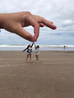 two girls standing on the beach with their hands in the air and one girl reaching for her hand