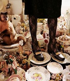 a woman standing in front of a pile of plates and other items on the floor