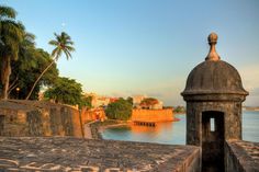 an old stone building with a dome on top next to the water and palm trees