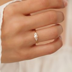 a woman's hand wearing a gold ring with pearls on the middle and a pearl bead in the middle