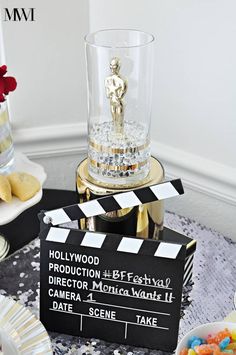 a movie clapper sitting on top of a table next to a glass filled with candy