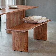 a wooden bench with a pillow on top of it next to a table and chair