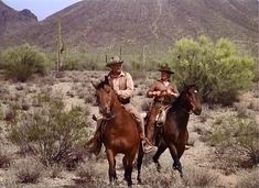 two men are riding horses in the desert