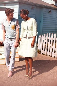 a man and woman standing in front of a white picket fence with a house behind them