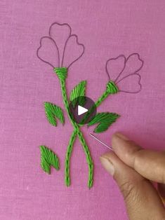 someone is stitching flowers with green thread on a pink surface and the video appears to be playing