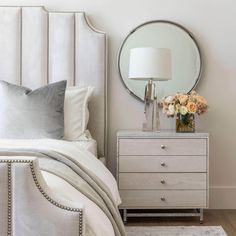 a white bed sitting next to a mirror on top of a dresser in a bedroom