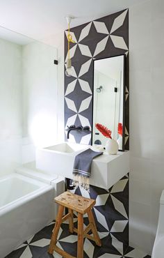 a bathroom with black and white tiles on the wall, a wooden stool and a mirror