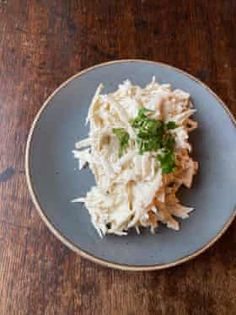 a blue plate topped with shredded chicken and garnished with parsley on a wooden table