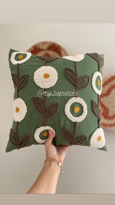 a hand holding a green pillow with white flowers on it