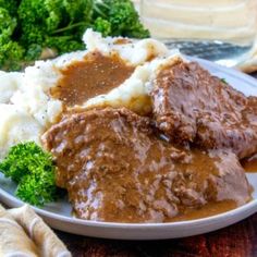 a white plate topped with meat and gravy next to asparagus