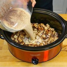 a person pouring something into a crock pot filled with food on top of a wooden table