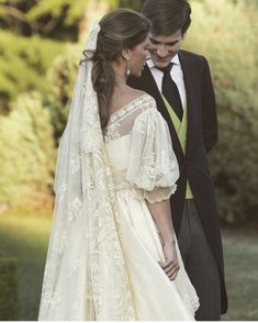 a man and woman standing next to each other in front of bushes wearing wedding gowns