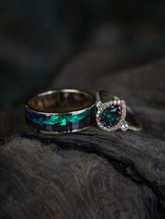 Two unique wedding rings from Staghead Designs sit on a piece of driftwood. These rings are inspired by Aurora Borealis, or the Northern Lights. On the left is a 14K yellow gold wedding band with dark maple wood mountains & an indigo sky made of opal & glow-in-the-dark powder. On the right is a 14K yellow gold "KB" engagement ring with a pear cut lab-created alexandrite center stone & diamond halo & accents. Engraved Wedding Ring, Engraved Wedding Rings, Staghead Designs, Cute Engagement Rings, Future Engagement Rings, Alexandrite Engagement Ring, Engraved Wedding, Men's Wedding Ring, Dream Engagement Rings