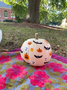 a painted pumpkin sitting on top of a colorful blanket in front of a large tree