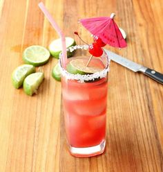 a red drink sitting on top of a wooden table next to limes and a knife