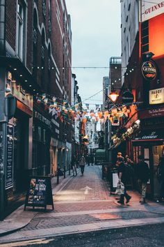 a city street with people walking down it and lights strung from the buildings above them