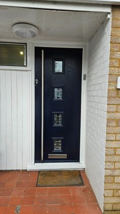 a black front door on a white brick house with red tile flooring and an entrance mat