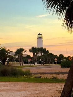 a white light house sitting on top of a lush green field next to palm trees