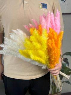 the man is holding three colorful feathers in his hand and wearing a tan polo shirt