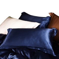 a pile of blue and white pillows on top of a bed covered in satin material