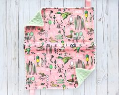 a pink and green pot holder with cactus print on the front, sitting against a white wooden wall