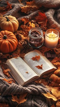 an open book sitting on top of a pile of leaves next to a lit candle