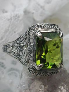 Simulated Green Peridot Ring Autumn Design #D200 Inspired by Victorian era designs, this lovely filigree reproduction has been recreated in sterling silver. This flawless 5 carat simulated Green Peridot gemstone is 12mm x10mm in size. The ring sits 17mm (11/16") North to South on the finger. The inside of the band is etched 925 for sterling silver. Notice the intricate and detailed design of the antique silver filigree setting all the way down the band. This is an exquisite rendition of an antiq Classic Green Filigree Ring With Gemstone, Elegant Filigree Ring For May Birthstone, Elegant Rectangular Peridot Rings, Classic Green Filigree Ring Hallmarked, Green Sterling Silver Classic Filigree Ring, Elegant Filigree Ring With May Birthstone Gemstone, Classic Green Sterling Silver Filigree Ring, Elegant Filigree Ring As May Birthstone Gift, Green Filigree Ring With Intricate Design For Wedding