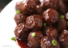 a white plate topped with meatballs covered in sauce and garnished with green onions