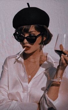 a woman holding a wine glass in her right hand and wearing a hat on top of her head